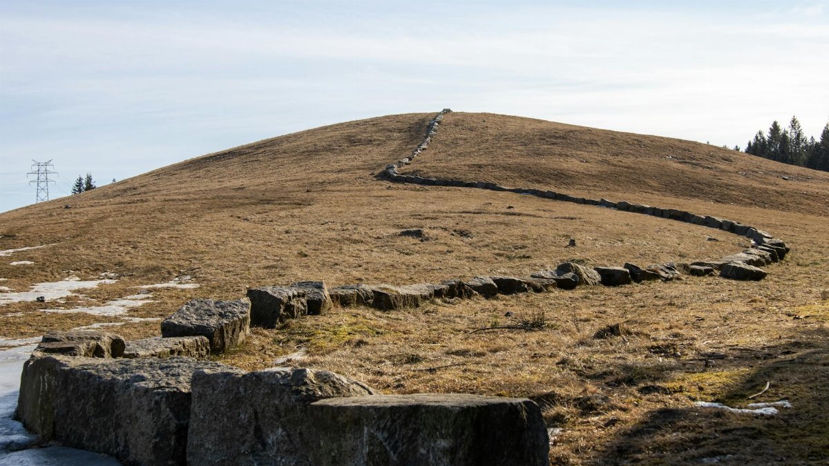 Stonewall winding on a hill in Spydeberg, Norway under a cloudy sky, showcasing natural beauty.