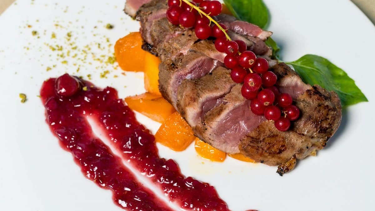Sliced duck breast served with red currant sauce, enhancing a gourmet dining experience.