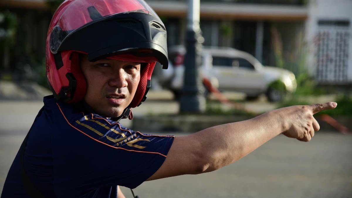 A man wearing a helmet points with his finger outdoors, seeming to direct attention or traffic.