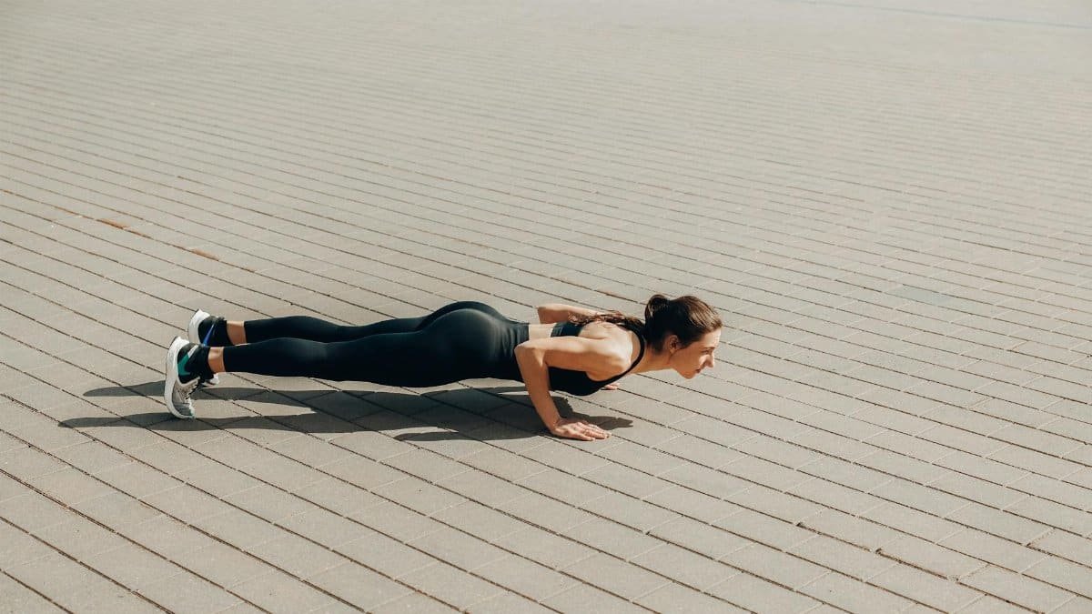 Fit woman in activewear performing push-ups outdoors on a sunny day.