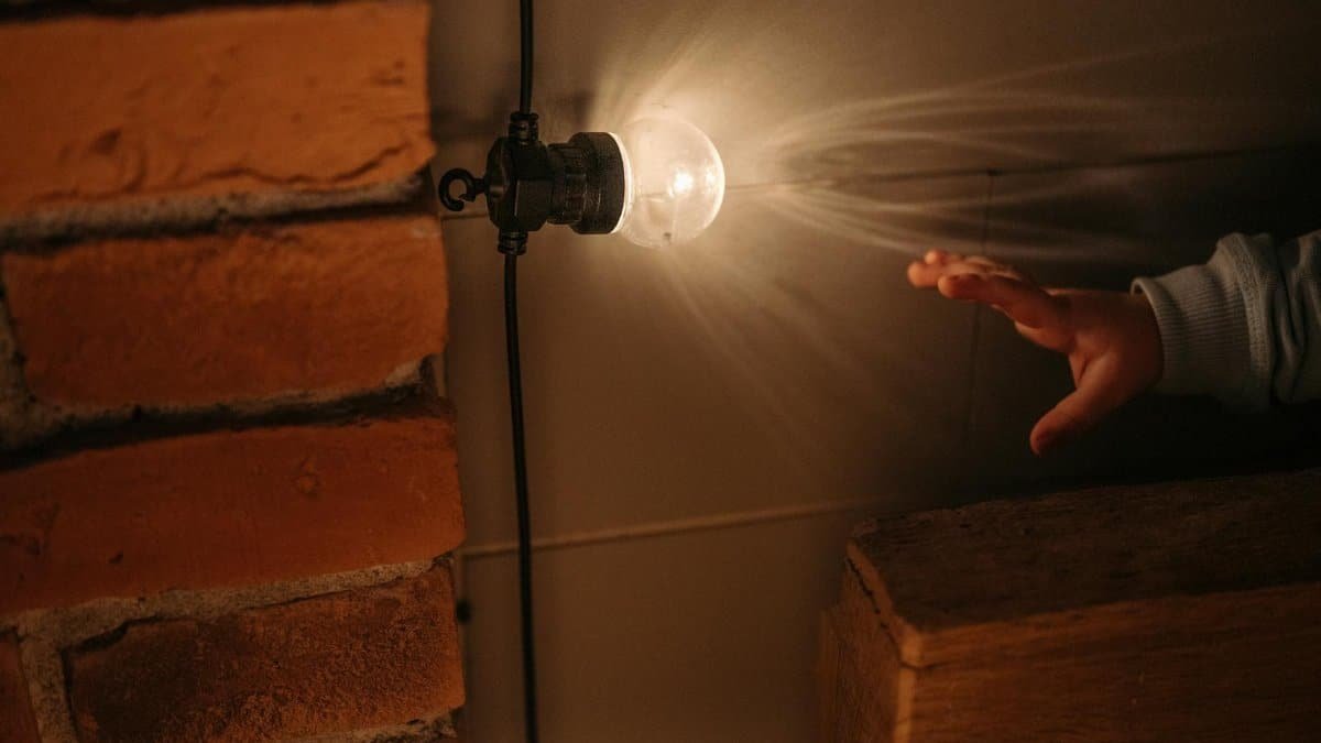 A young child's hand reaching towards a warm glowing vintage bulb set against a brick wall.