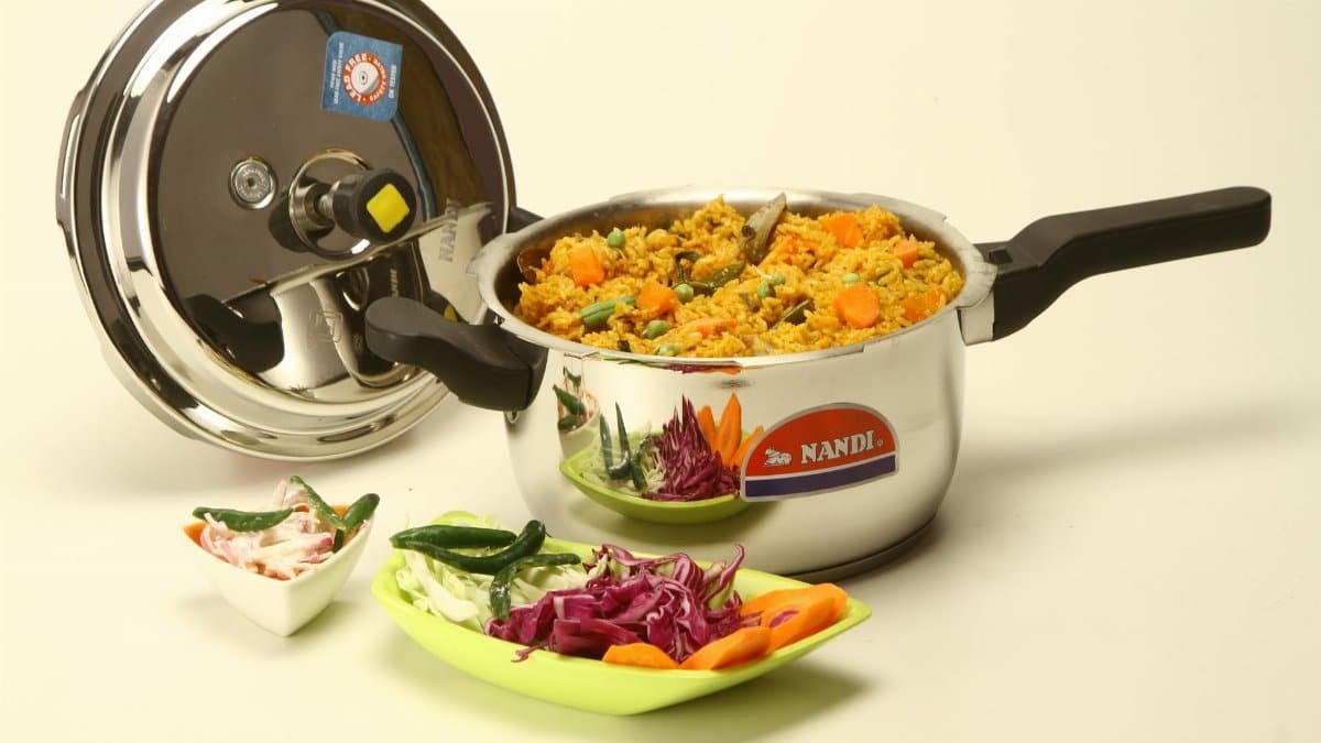 Colorful vegetable biryani cooked in a stainless steel pressure cooker with fresh ingredients.