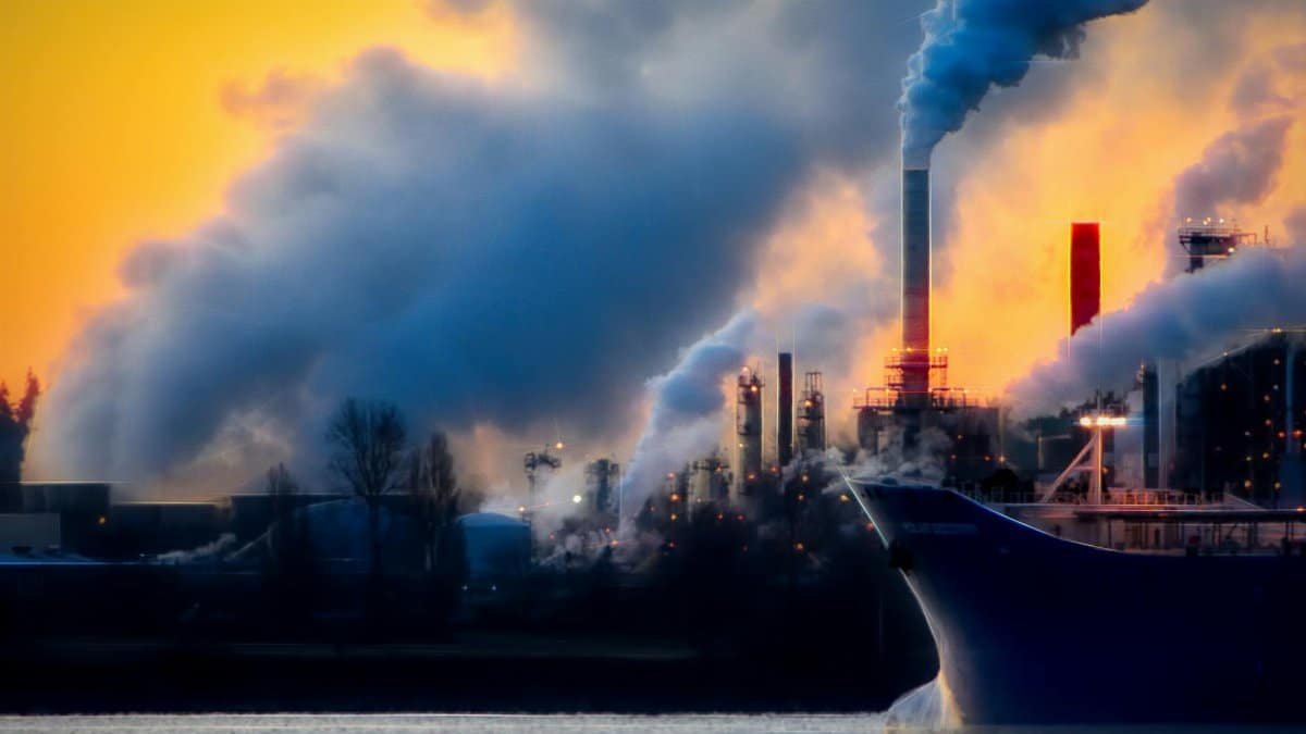 A factory emits thick smoke and pollution against a vibrant sunset, highlighting industrial impact on the environment.