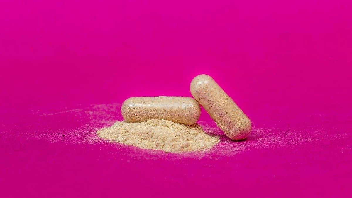 Close-up of two supplement capsules and powder on a vibrant pink background.