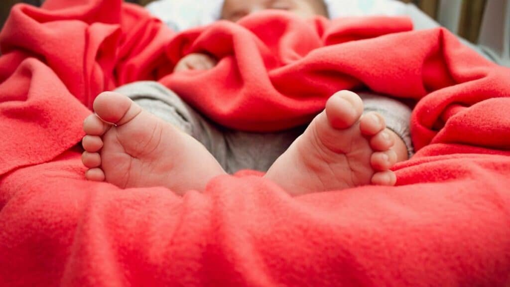 Adorable baby sleeping wrapped in a cozy red blanket, showing tiny feet.
