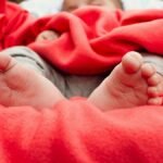 Adorable baby sleeping wrapped in a cozy red blanket, showing tiny feet.