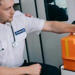 Paramedic sitting in an ambulance with an orange medical kit, ready for emergency response.