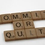 Wooden Scrabble tiles arranged to form the words 'Commit or Quit' on a white background.
