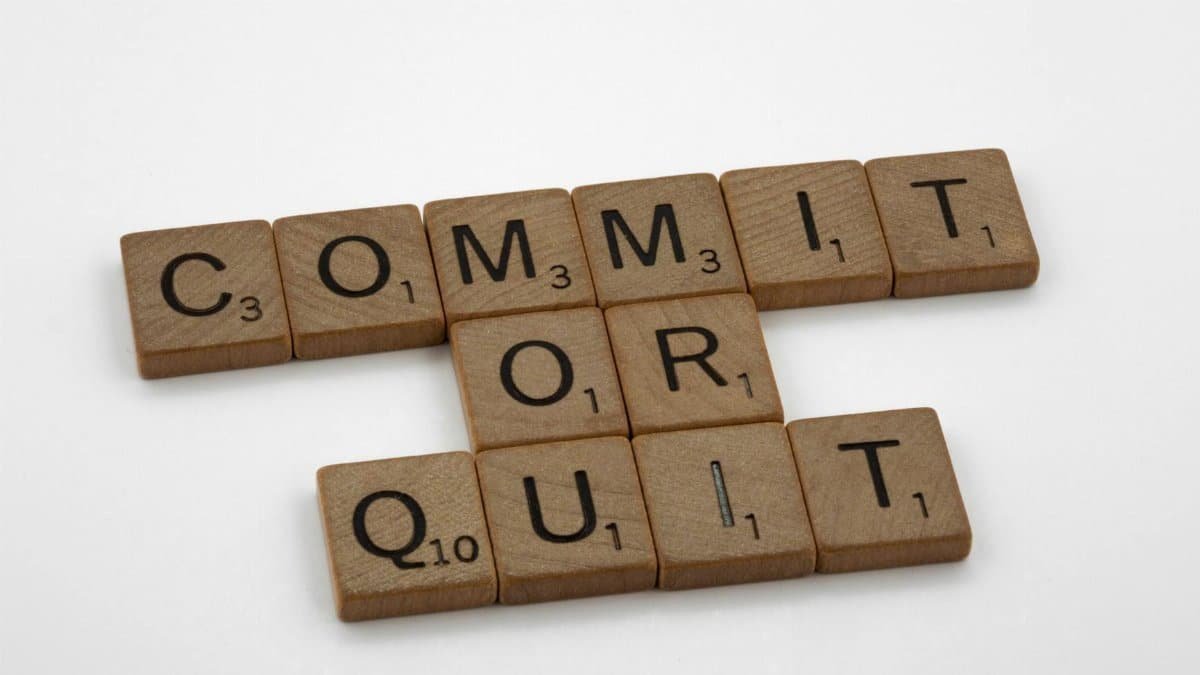 Wooden Scrabble tiles arranged to form the words 'Commit or Quit' on a white background.