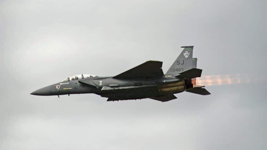 Dramatic view of F-15 fighter jet flying outdoors, showcasing afterburners against a cloudy sky.