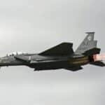 Dramatic view of F-15 fighter jet flying outdoors, showcasing afterburners against a cloudy sky.