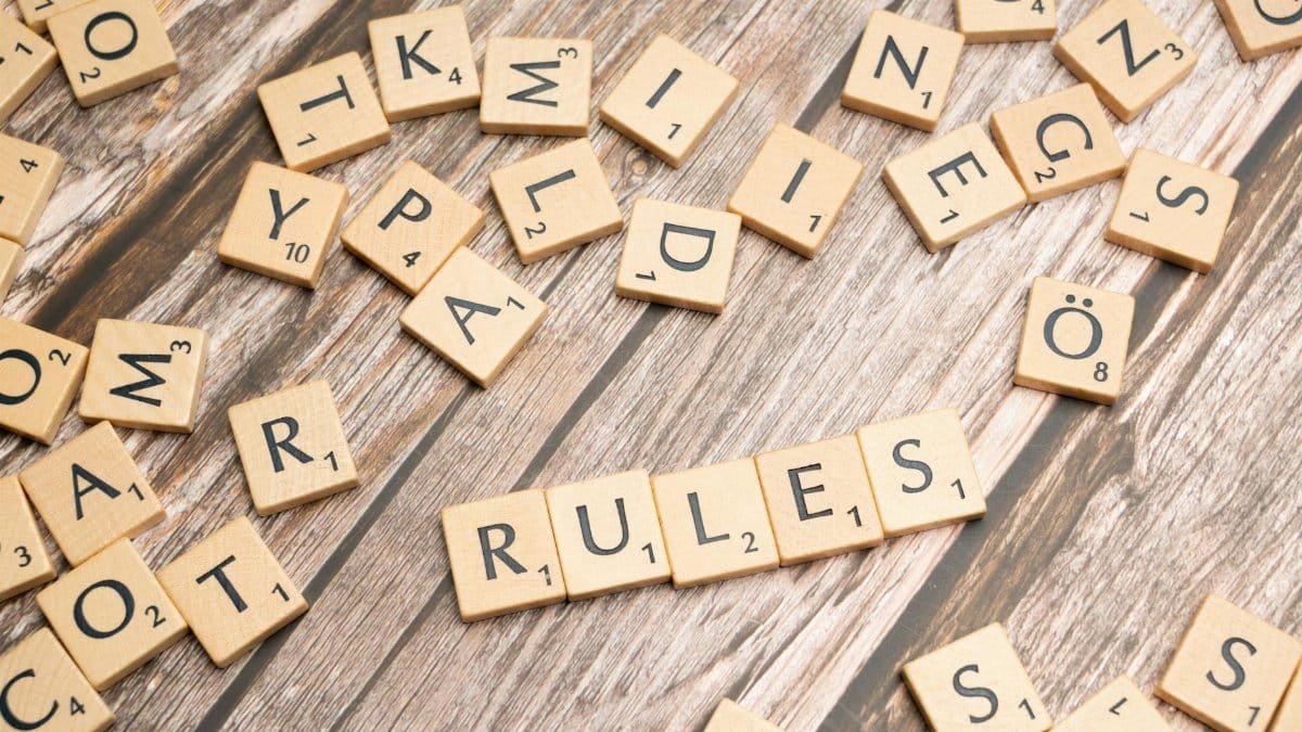 Wooden letter tiles arranged to spell 'Rules' on a textured wooden background.
