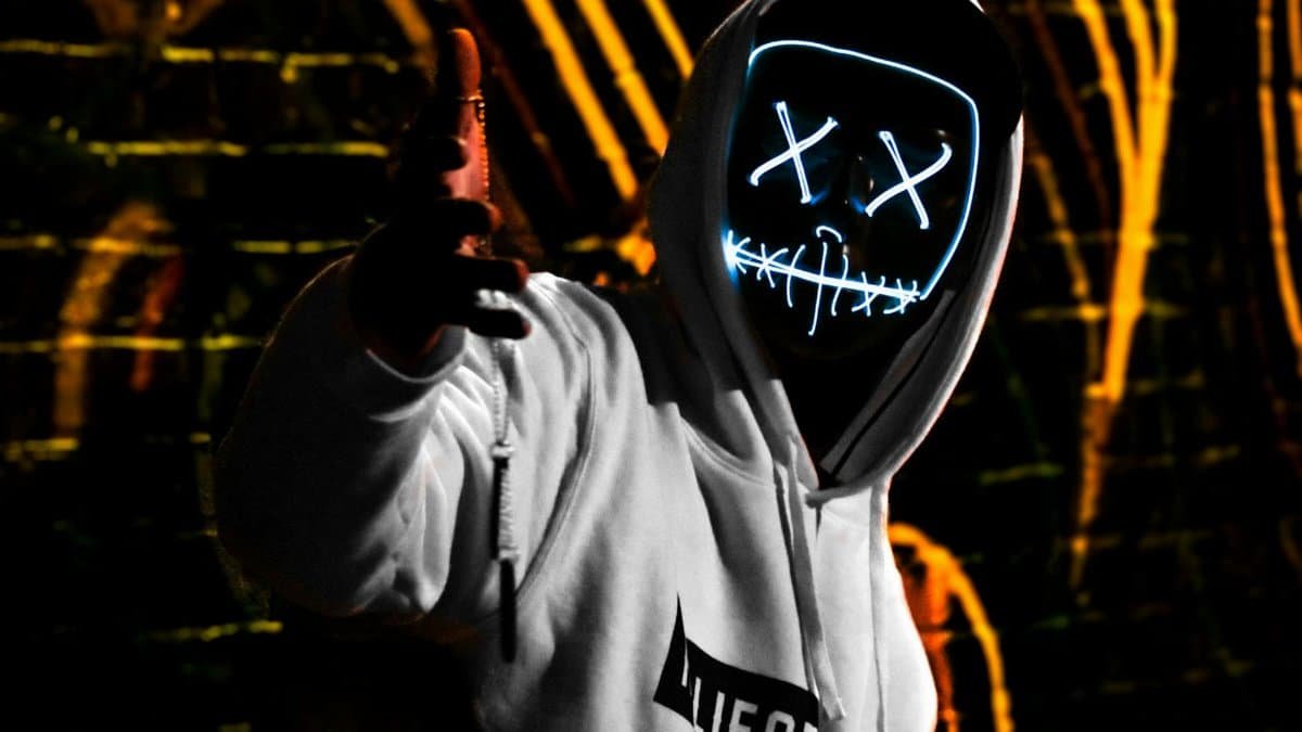 Hooded figure wearing a glowing LED mask in an urban environment at night.
