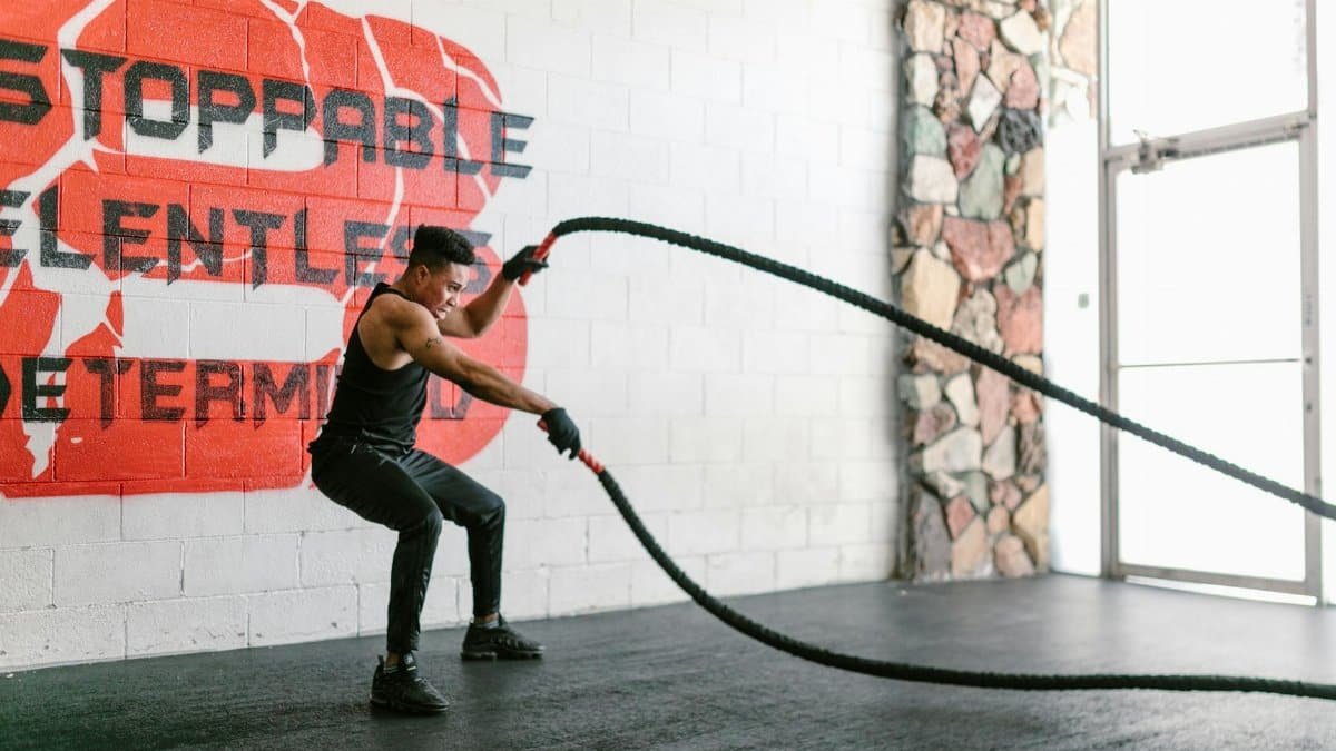 Athletic man training with battle ropes in a gym with motivational wall art.