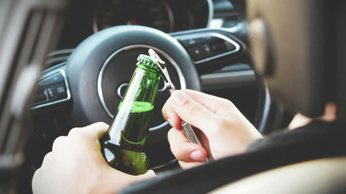 Hands opening a beer bottle inside a car, highlighting the importance of safe driving and awareness of road dangers.