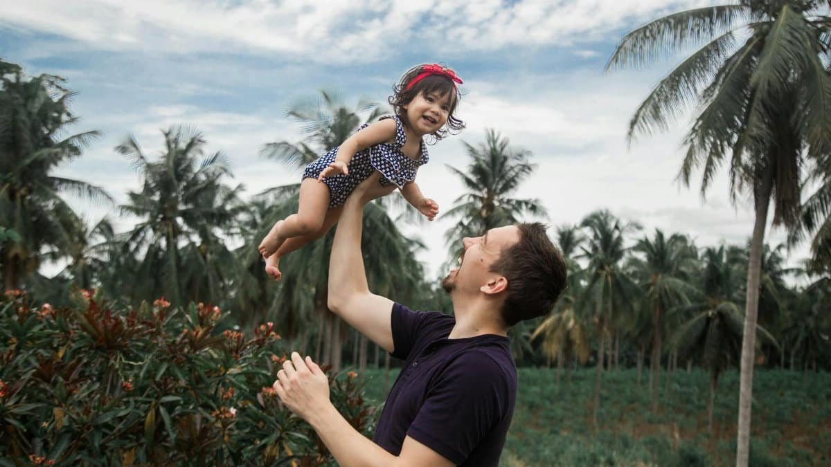 Father lifting his daughter joyfully amid a lush tropical landscape.