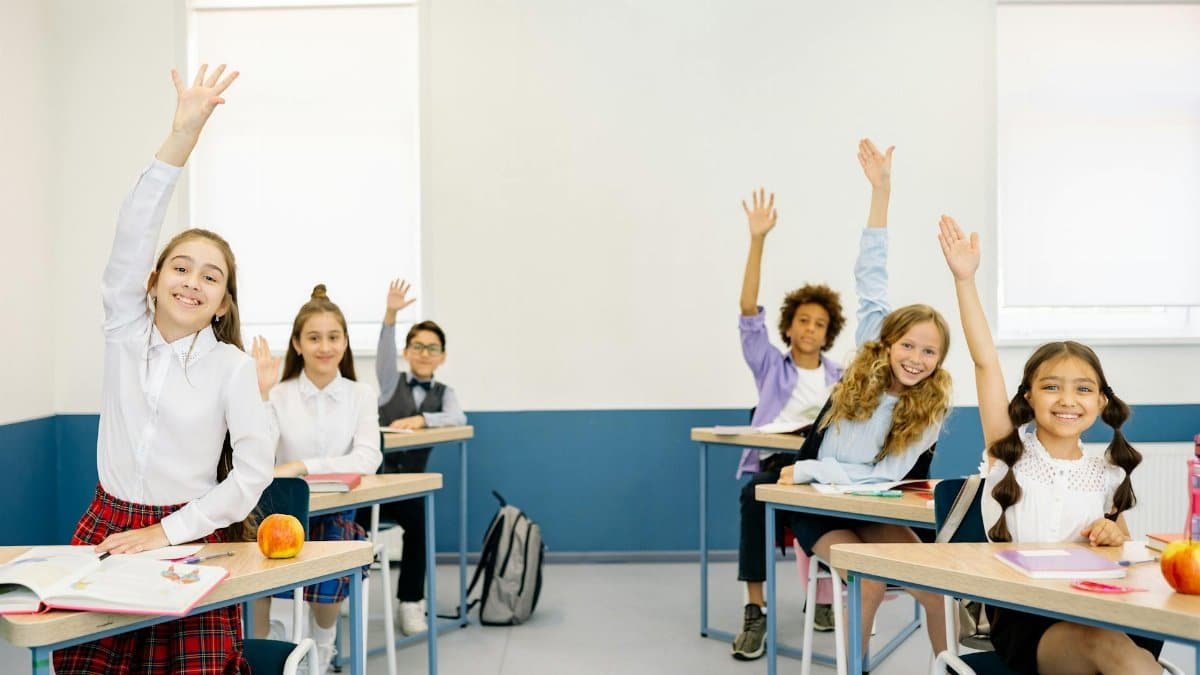 Group of diverse children eagerly raising hands in a bright classroom setting.