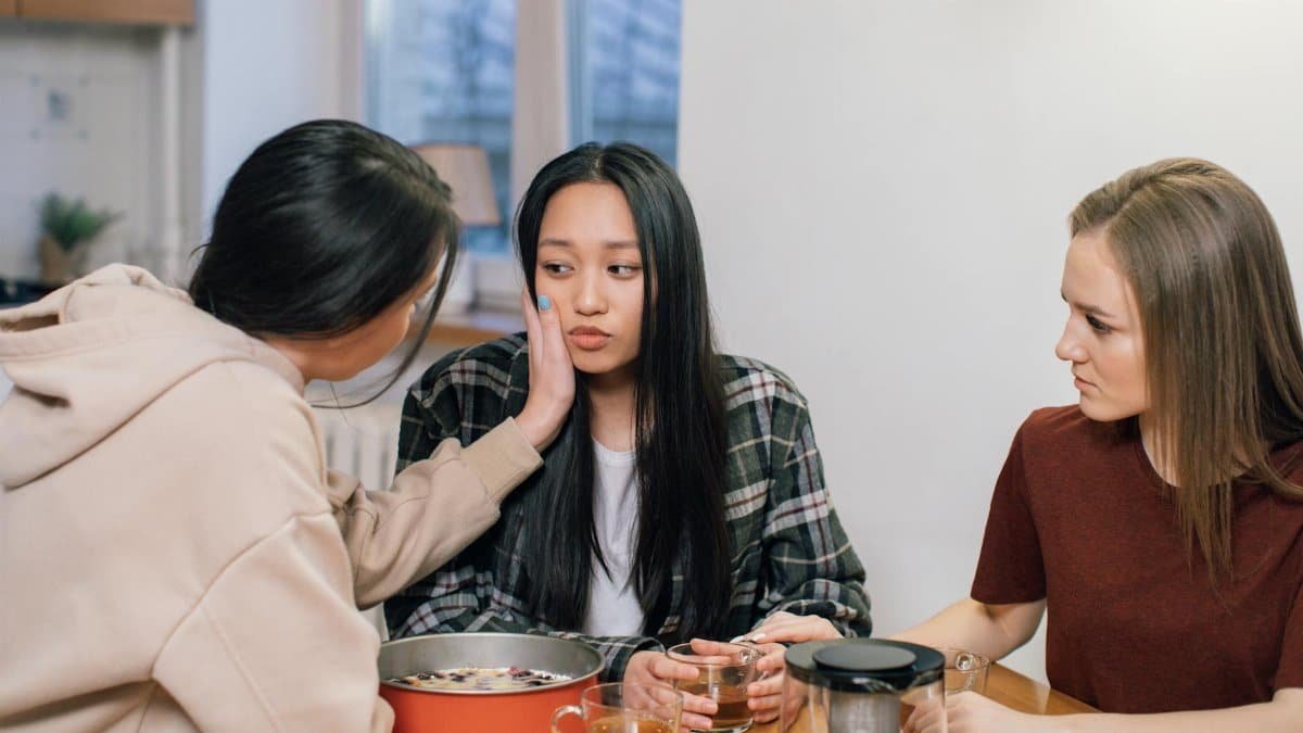 Three women at a table offering emotional support and comfort to a friend, fostering compassion and empathy.