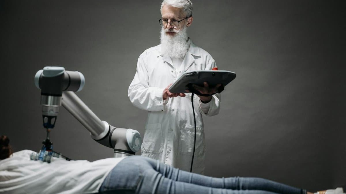 A scientist controls a robotic arm conducting research on a person lying down.