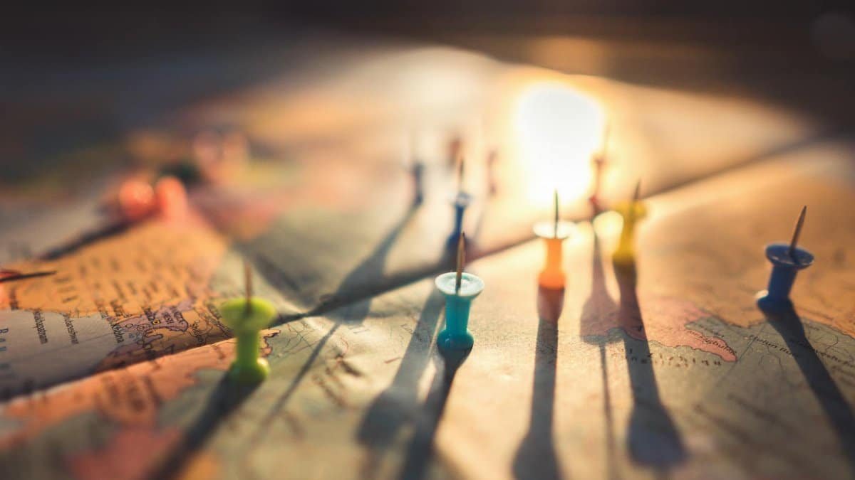 A close-up view of colorful push pins casting shadows on a world map during sunset, highlighting global travel.
