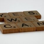 Scrabble tiles spelling 'Yes We Can' on a white background, conveying encouragement.