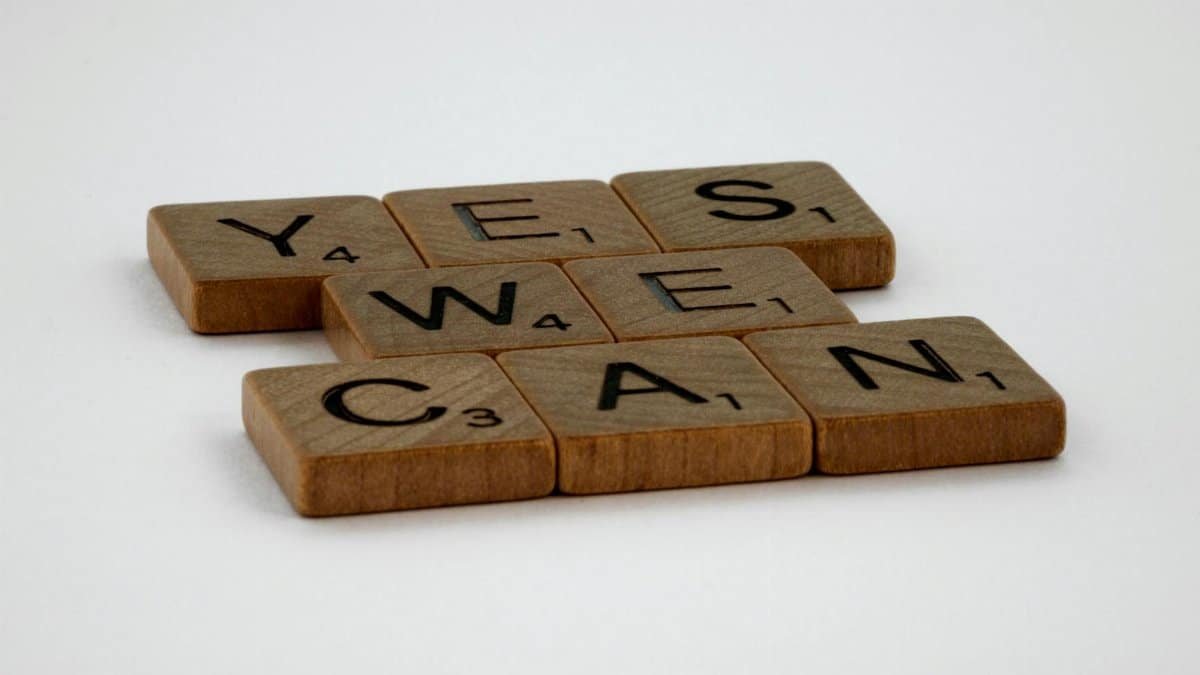 Scrabble tiles spelling 'Yes We Can' on a white background, conveying encouragement.