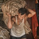 A man in Ballia, India, carrying heavy fabric bundles, showcasing hard work and determination.