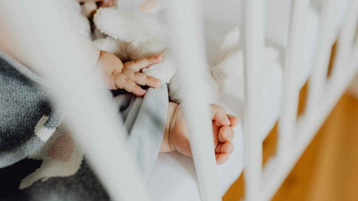 Adorable baby sleeping peacefully in a crib, holding a soft toy next to a baby blanket.