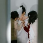 A bride getting ready with help from others, captured from behind in a bridal room.