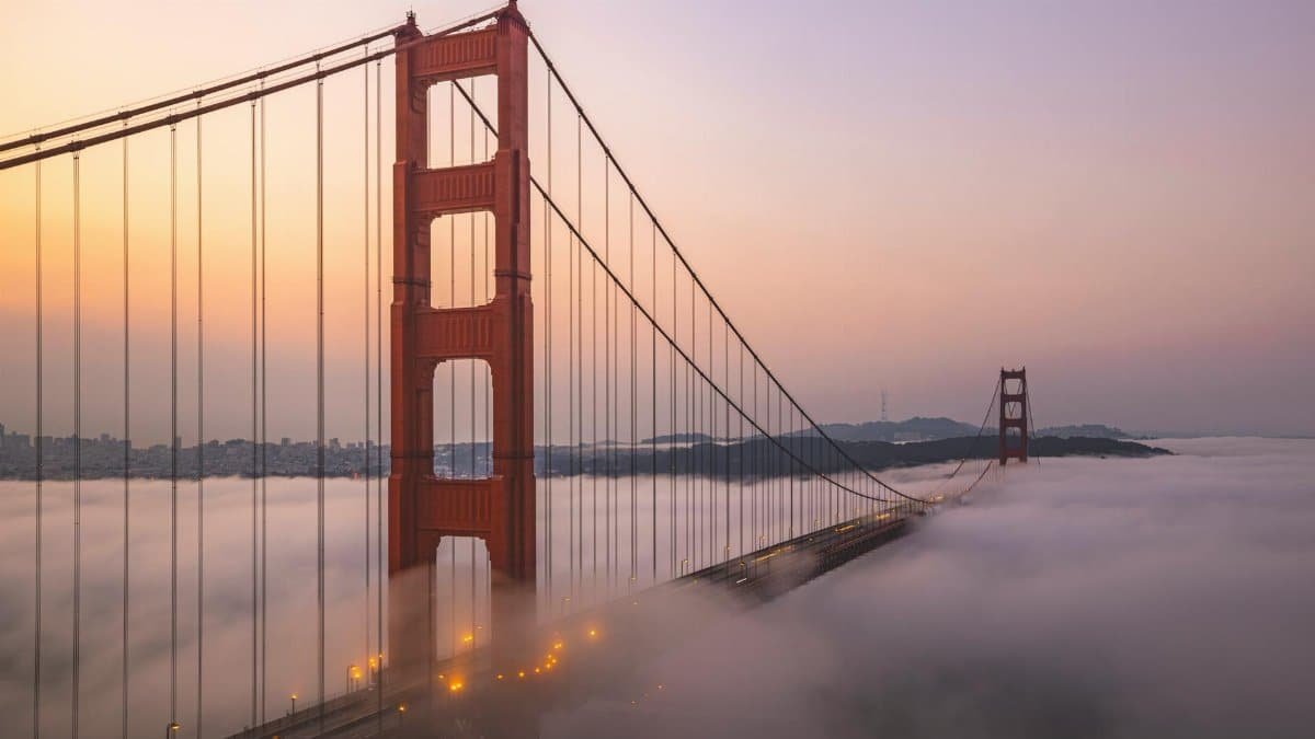 Aerial view of the Golden Gate Bridge enveloped in fog at sunrise.