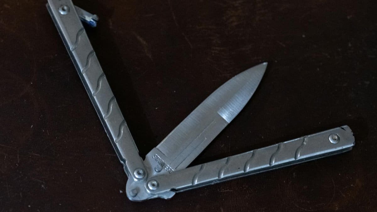 Detailed view of a silver balisong knife with open blade on a dark background, showcasing sharpness and design.