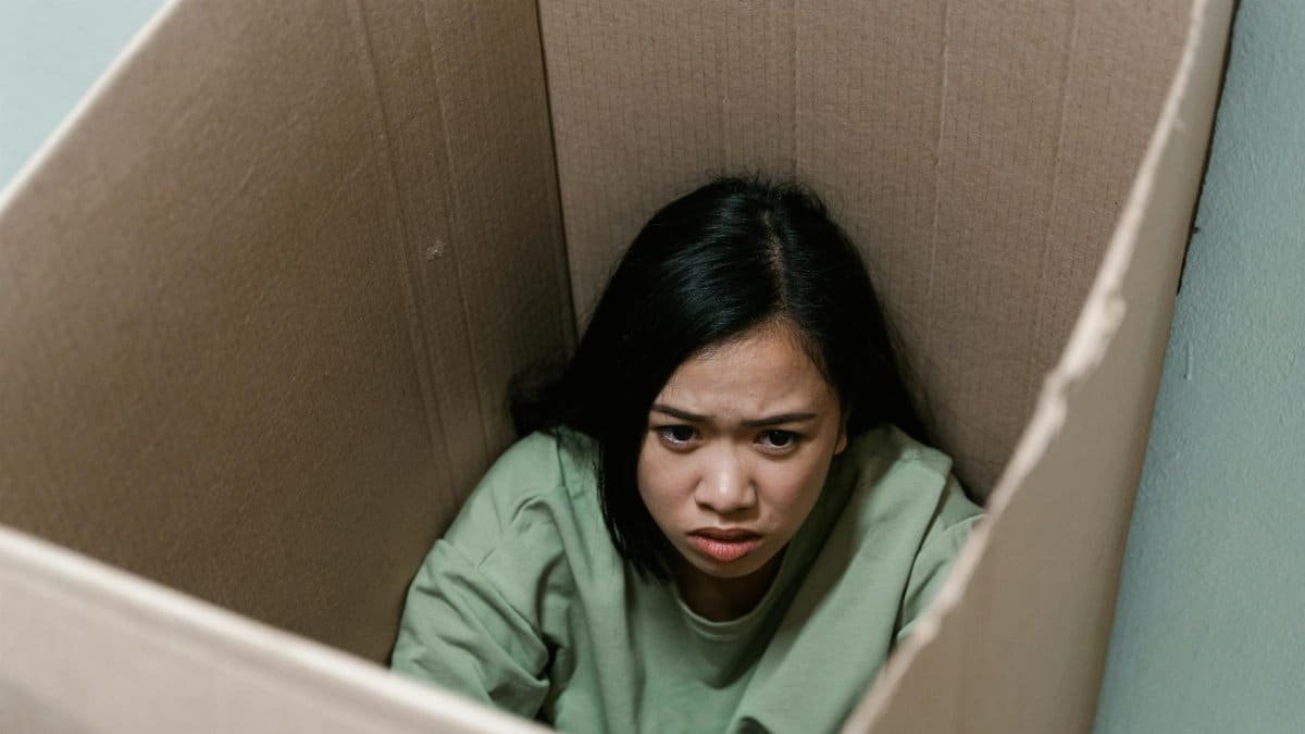 A woman inside a cardboard box symbolizes feelings of anxiety and claustrophobia.