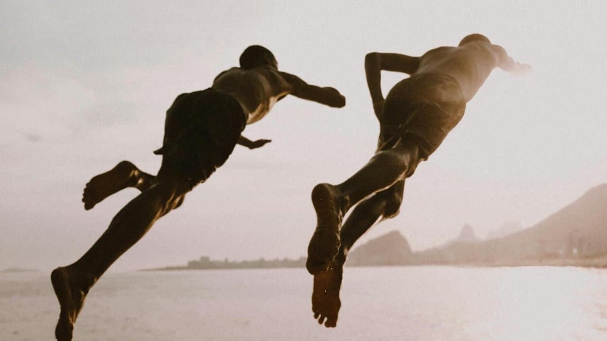 Two men leap into the sea at sunset in Rio de Janeiro, Brazil. Captured in dynamic motion.