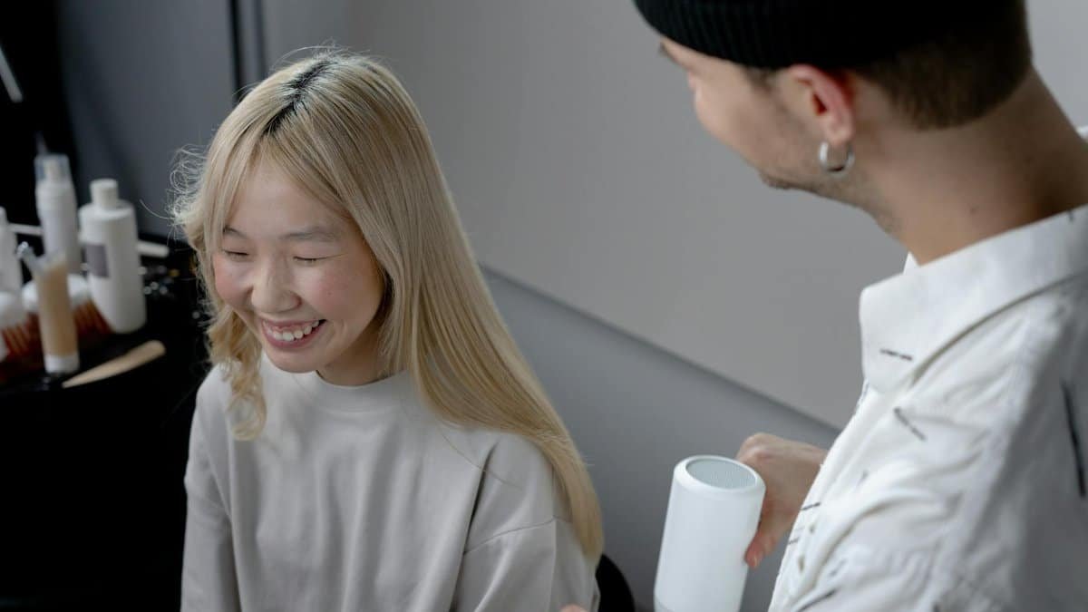 A hairstylist using a blow dryer on a smiling Asian woman in a hair salon.