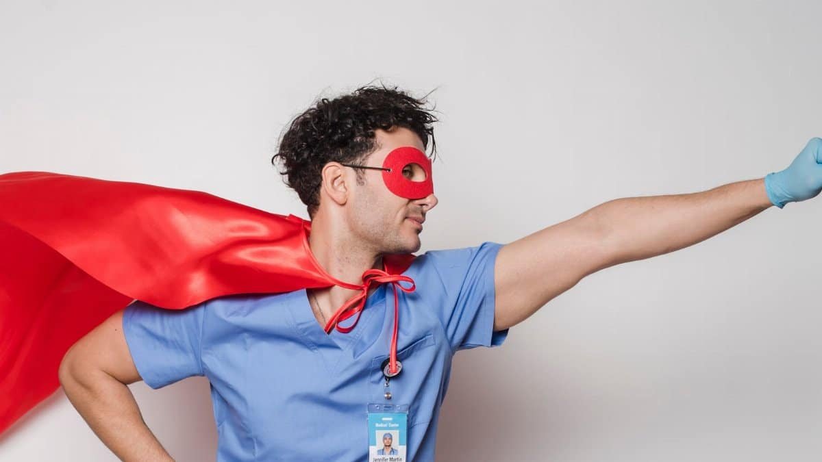 Male healthcare worker wearing a red cape and mask poses as a superhero. Studio shot.