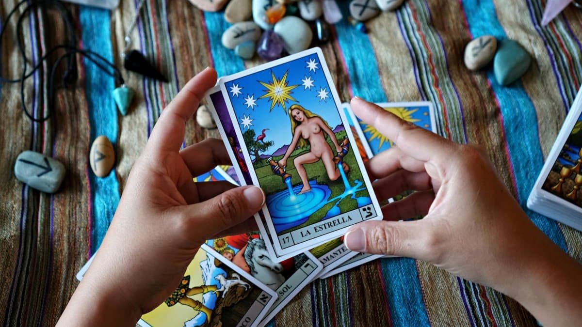Hands holding a La Estrella tarot card, surrounded by stones and other cards.