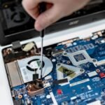 Hand repairing a laptop motherboard with a screwdriver, highlighting tech maintenance.