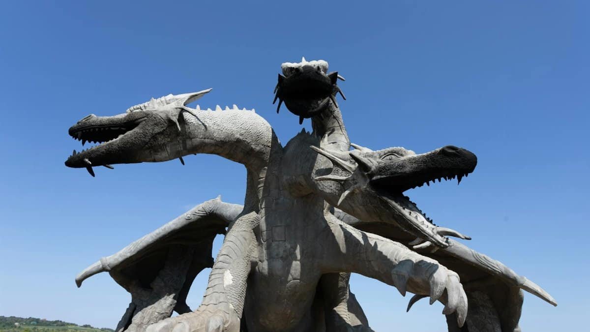 Three-headed dragon sculpture in an open landscape under a bright clear sky, showcasing intricate design and grandeur.