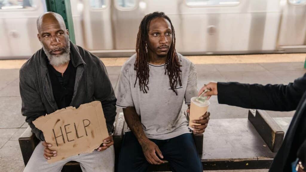 Two men in a subway station seeking help, with a passerby offering money.
