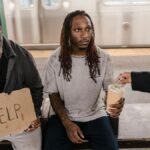 Two men in a subway station seeking help, with a passerby offering money.