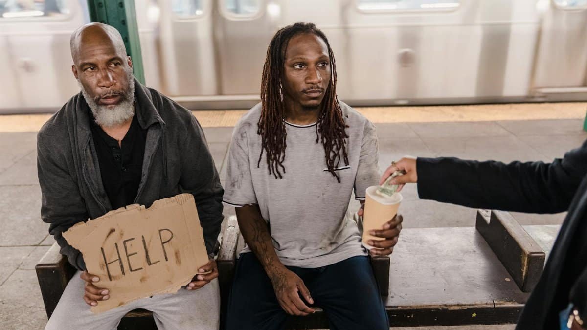 Two men in a subway station seeking help, with a passerby offering money.