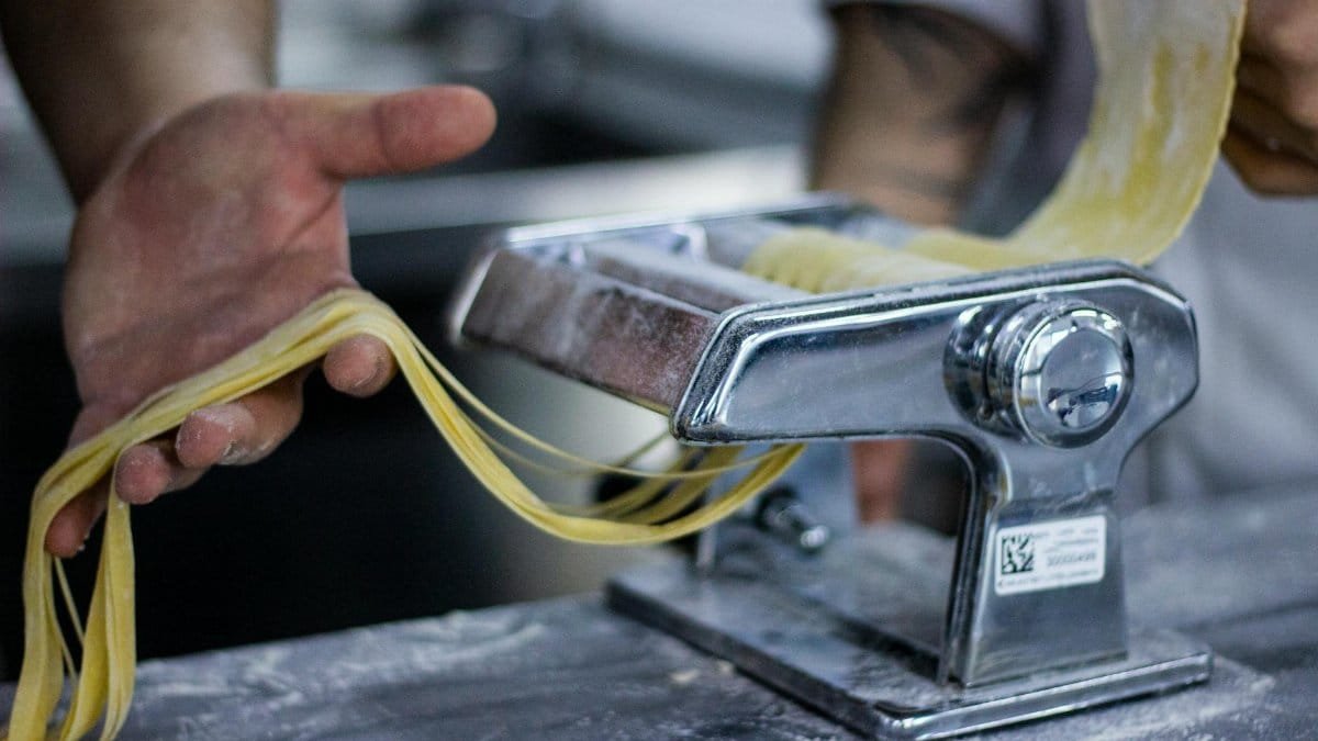 Close-up of fresh pasta being prepared with a manual pasta machine by hands in a kitchen.