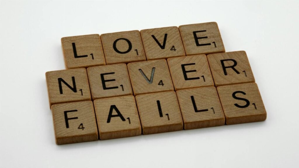 Wooden Scrabble tiles spelling out 'Love Never Fails' on a white background.