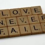 Wooden Scrabble tiles spelling out 'Love Never Fails' on a white background.