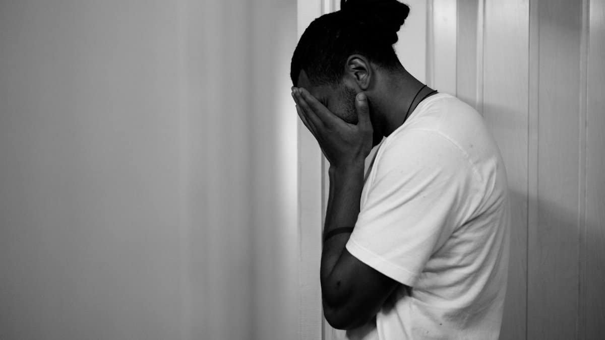 Black and white portrait of a man exhibiting stress, touching his face in an indoor setting.