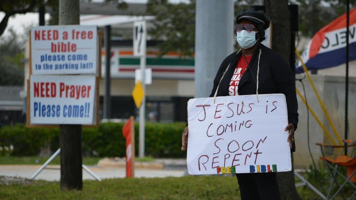 A person standing with a sign promoting religious messages in an urban setting.