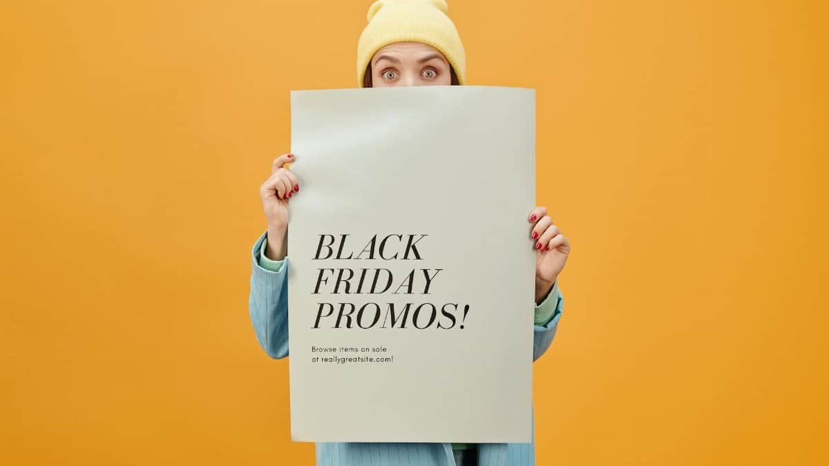 Person holding a Black Friday promo poster against a vibrant orange background. Ideal for sales and marketing concepts.