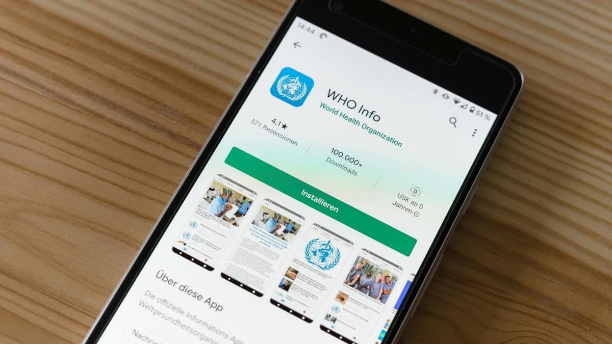 Mobile phone on wooden table showing installation screen for WHO Info app from World Health Organization.