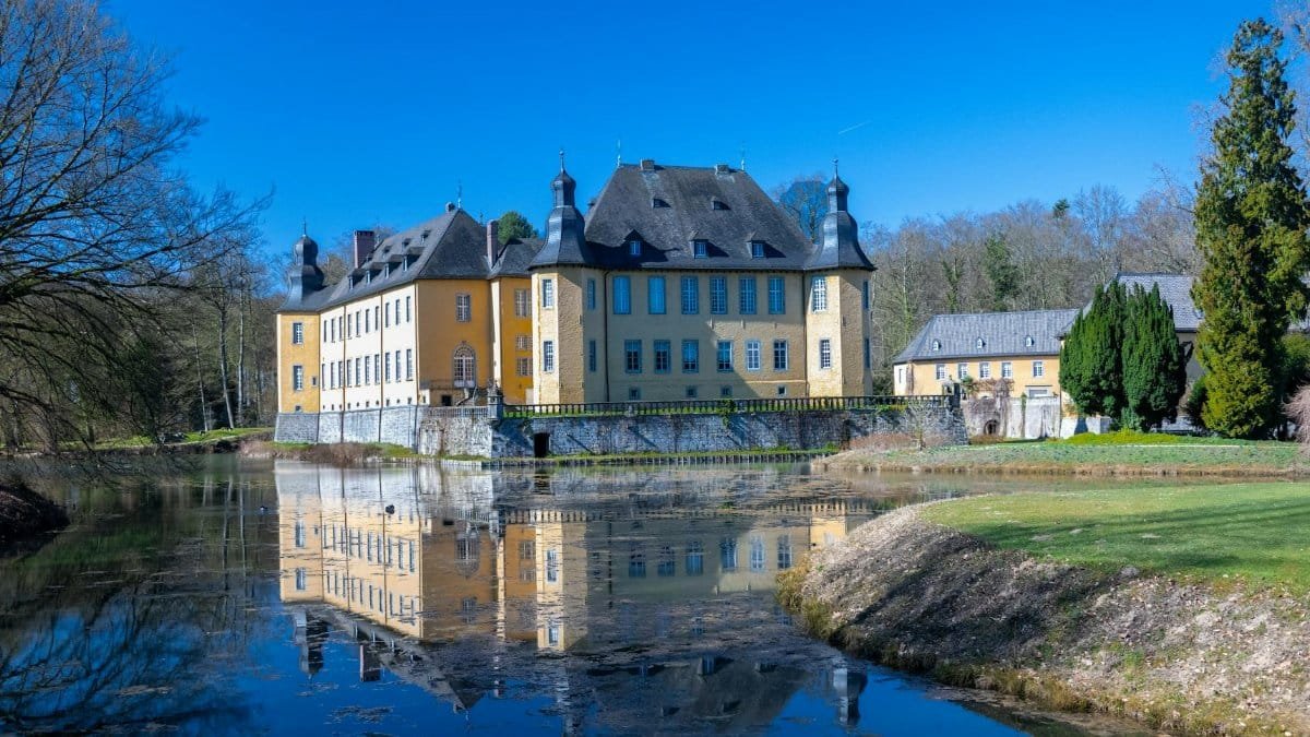 A stunning medieval castle with a moat reflecting under a blue sky.