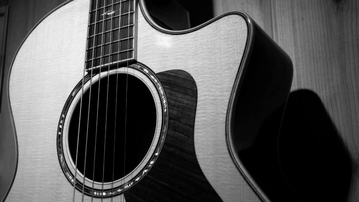 A detailed black and white close-up of a classic acoustic guitar, highlighting its strings and wood texture.